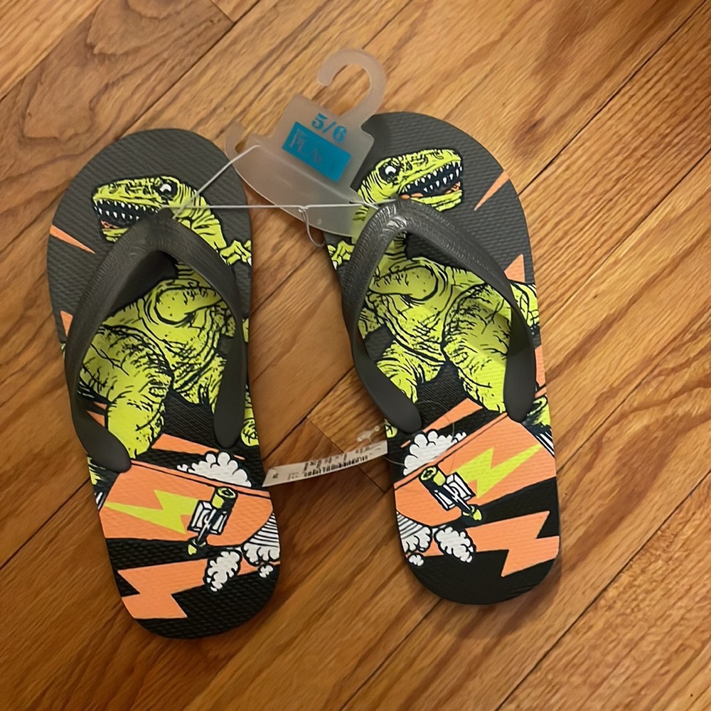 Children Place Dino print flip flops, size 5/6. Color gray, 100% plastic.